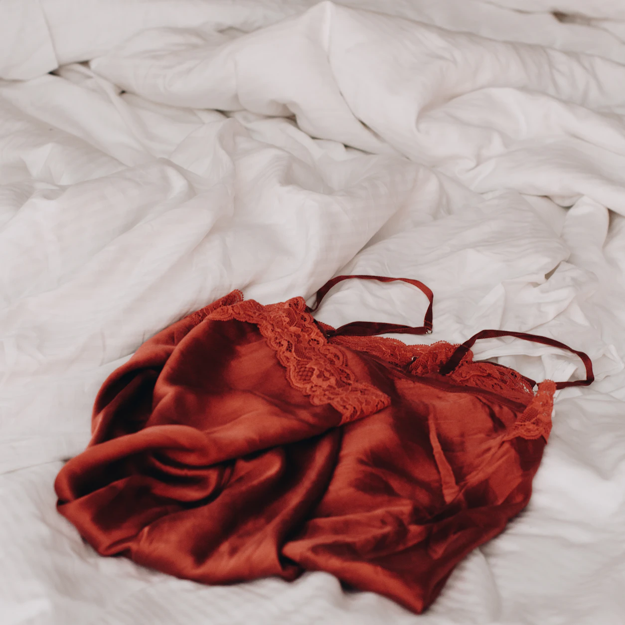 Lingerie vermelha sobre cama clara criando clima íntimo discreto e consensual